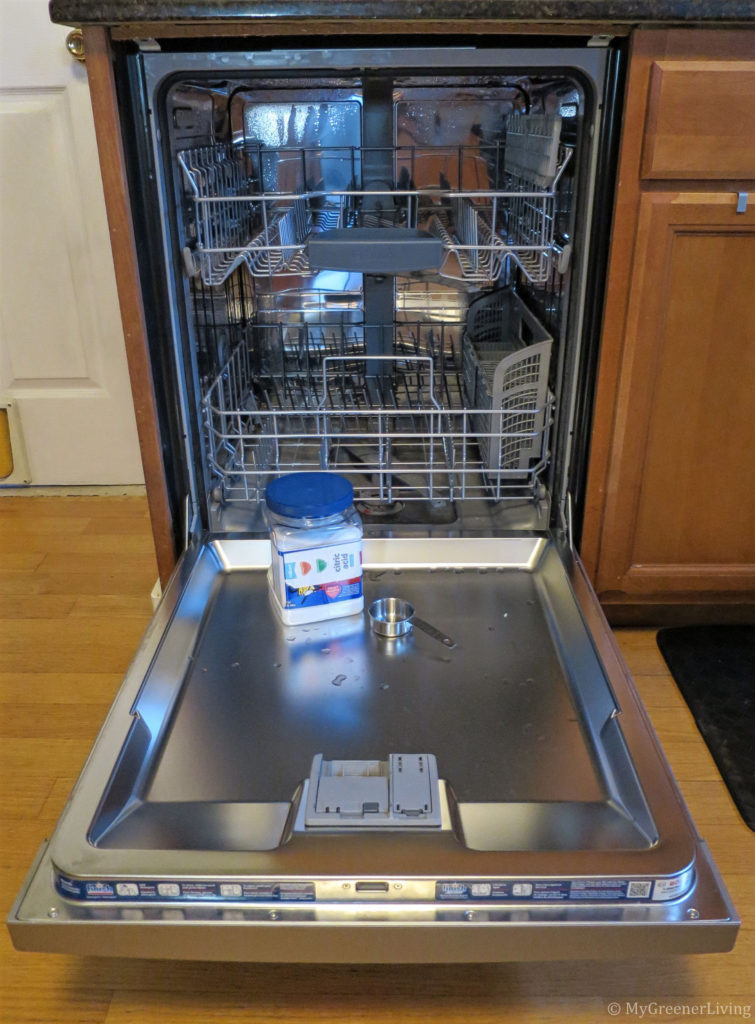 open dishwasher with container of citric acid and a 1/4 cup measuring cup