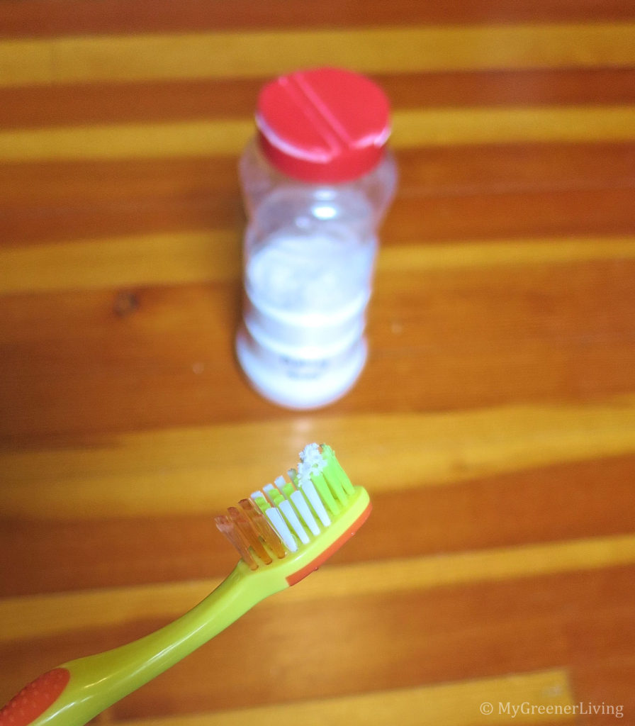 extra soft bristle toothbrush with a tiny bit of baking soda on the tip, with a jar of baking soda in the background.