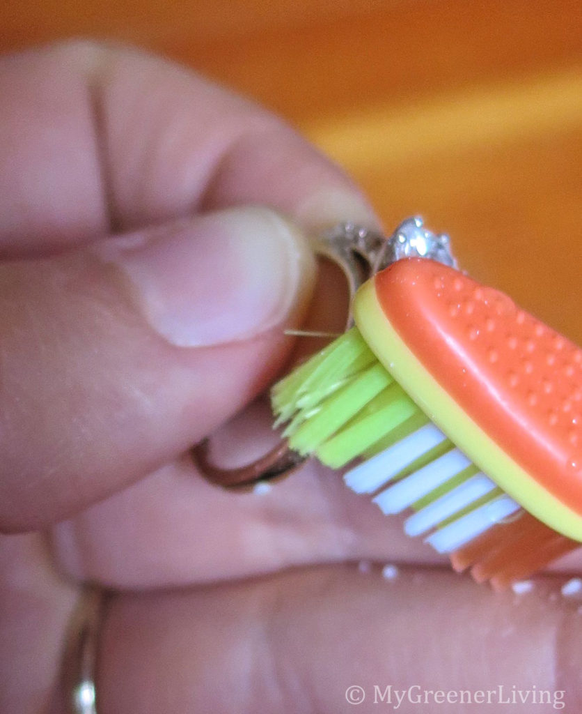 hand holding a ring, cleaning gemstone on a ring with baking soda and extra soft toothbrush
